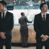 Two,Bodyguards,Waiting,For,Businessman,Standing,At,Reception,Counter