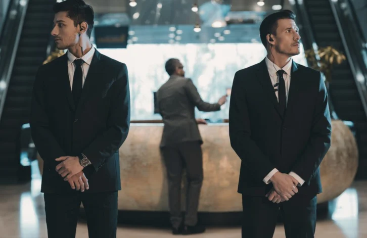 Two,Bodyguards,Waiting,For,Businessman,Standing,At,Reception,Counter
